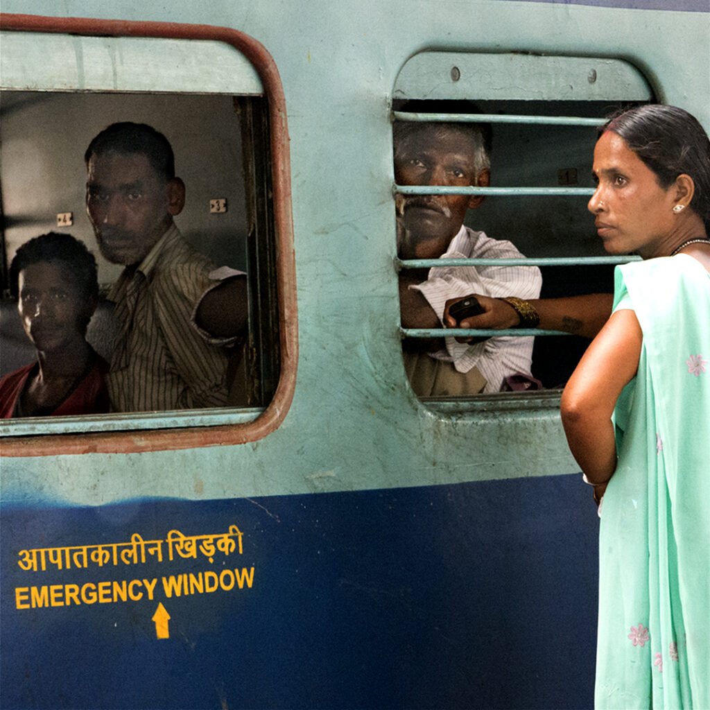Gare de Delhi, trois hommes dans un train fixent le photographe tandis qu'une femme sur le quai scrute l'horizon, en 2011.